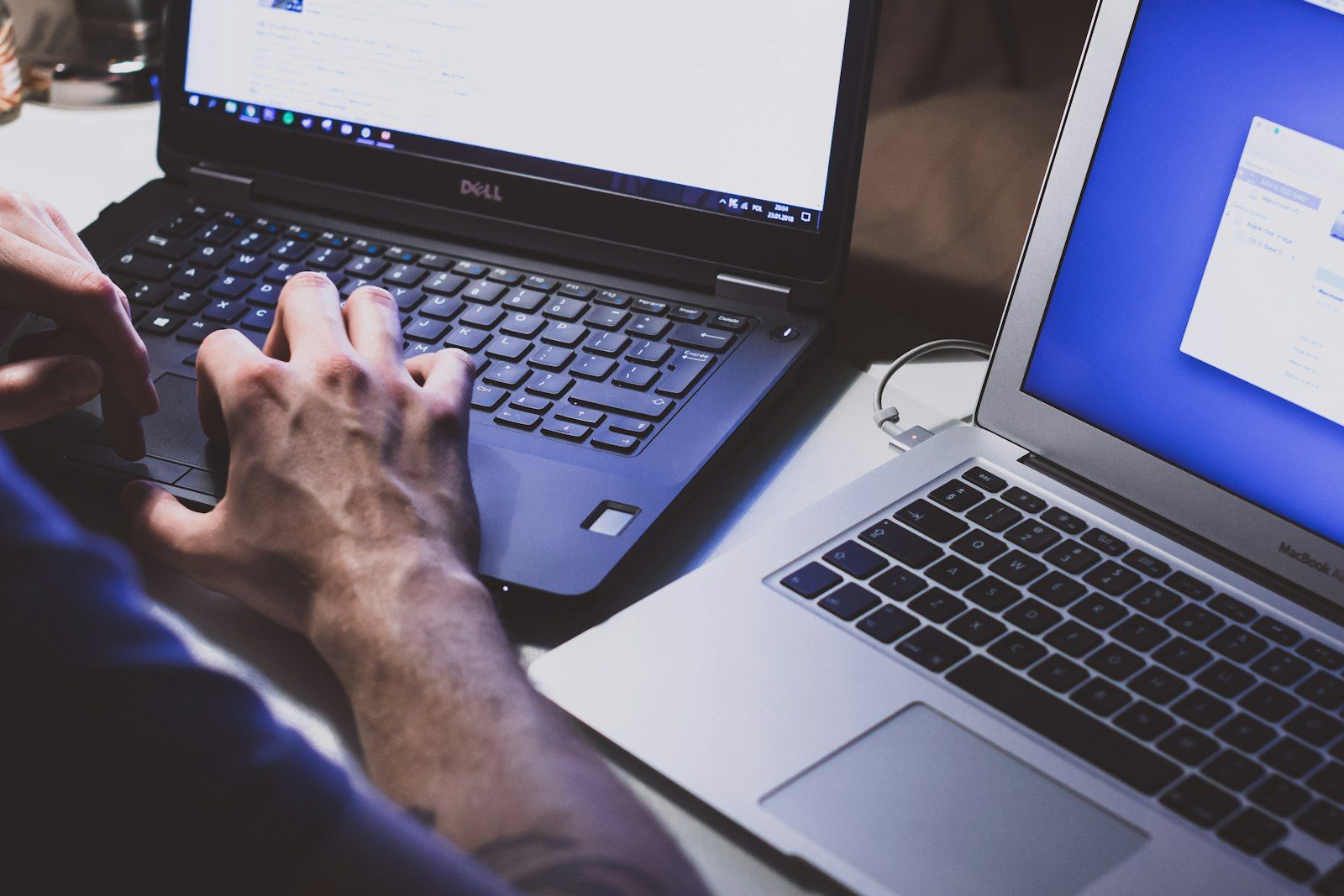 Hands typing on a laptop keyboard with a second laptop alongside