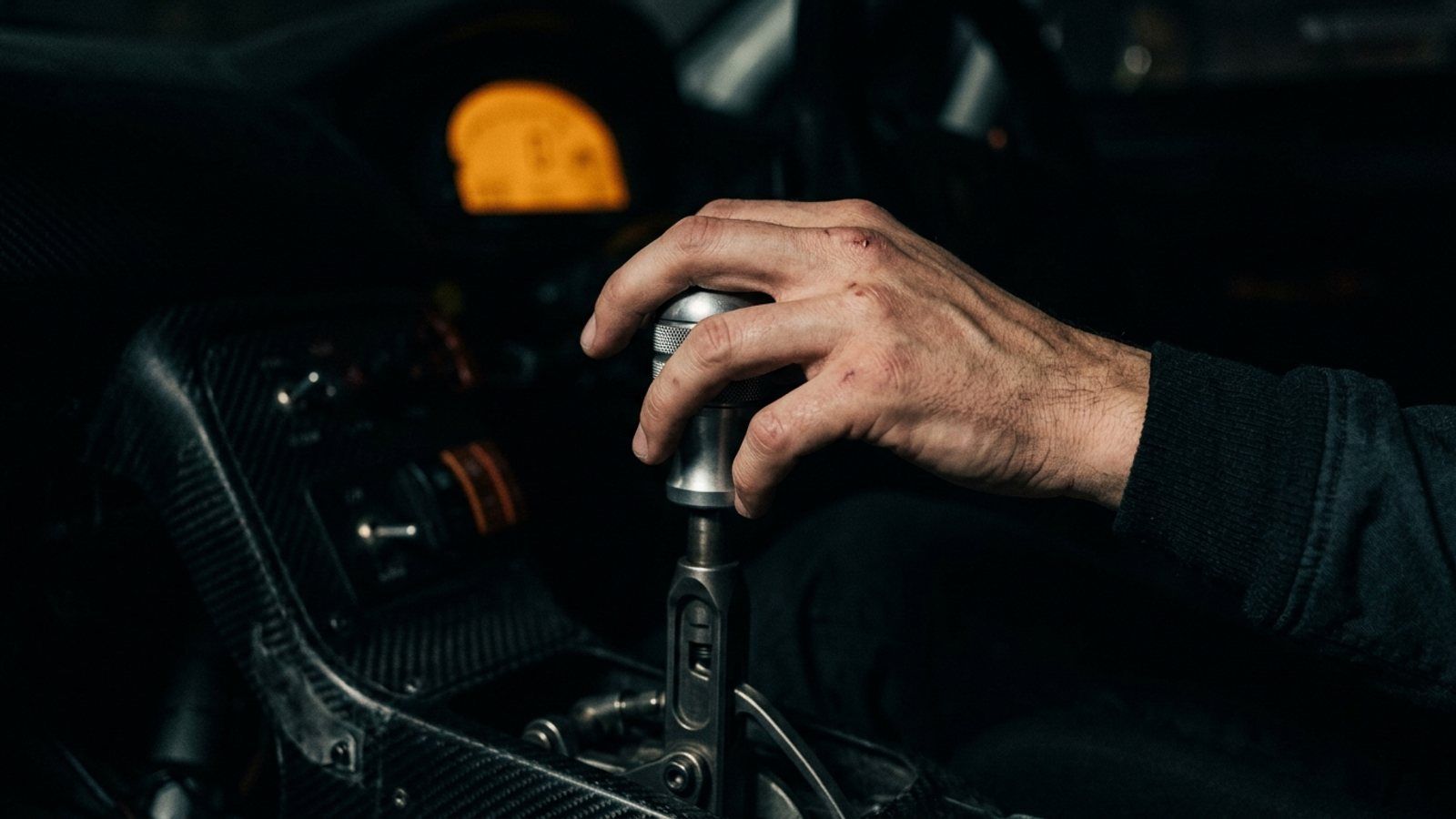 A hand resting lightly on a car's throttle, not pushing it down, under dramatic low light.